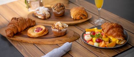 Una mesa de madera con pasteles, una ensalada de frutas y un vaso de zumo de naranja.
