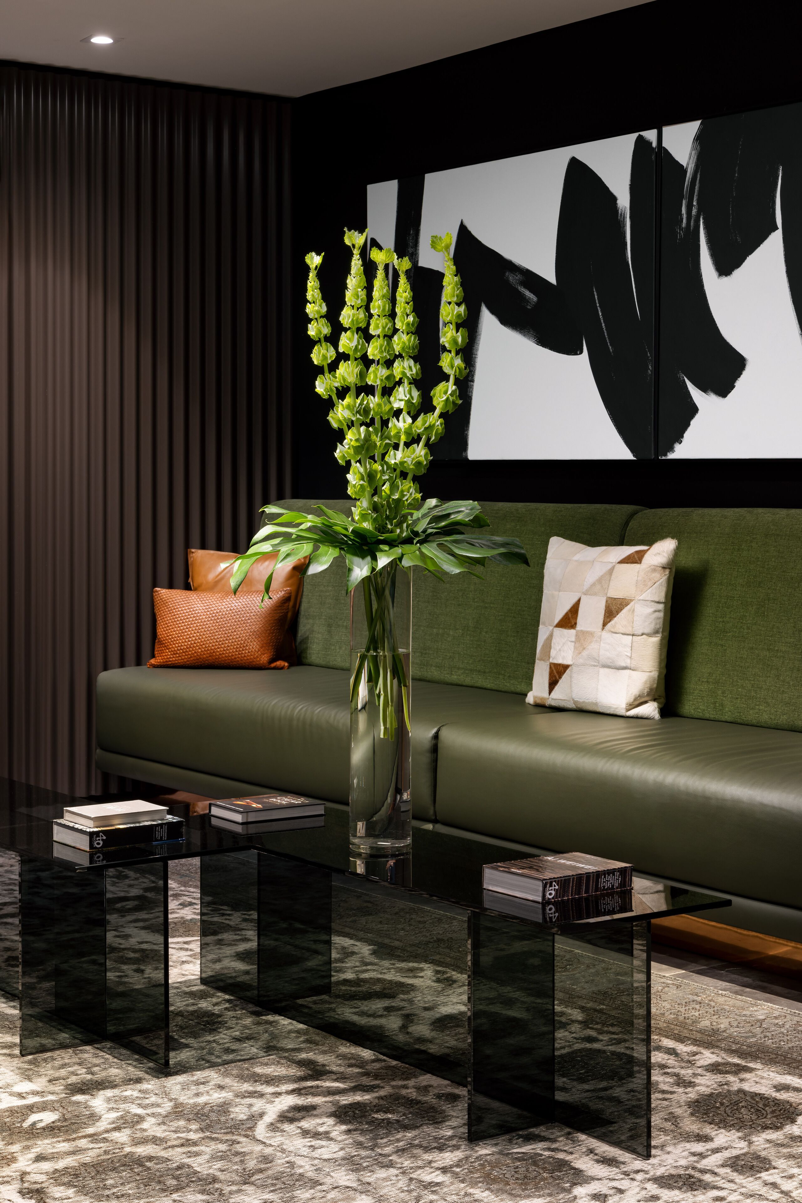 Un salon moderne avec un canapé vert, un vase contenant des plantes vertes et un tableau abstrait noir accroché au mur.