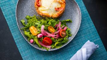 A plate with a baked item and a salad on a textured blue mat.