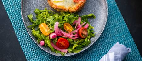 A plate with a baked item and a salad on a textured blue mat.