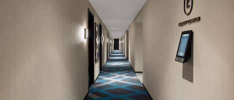 A hotel hallway with a patterned carpet, a request elevator sign, and a digital elevator control panel.