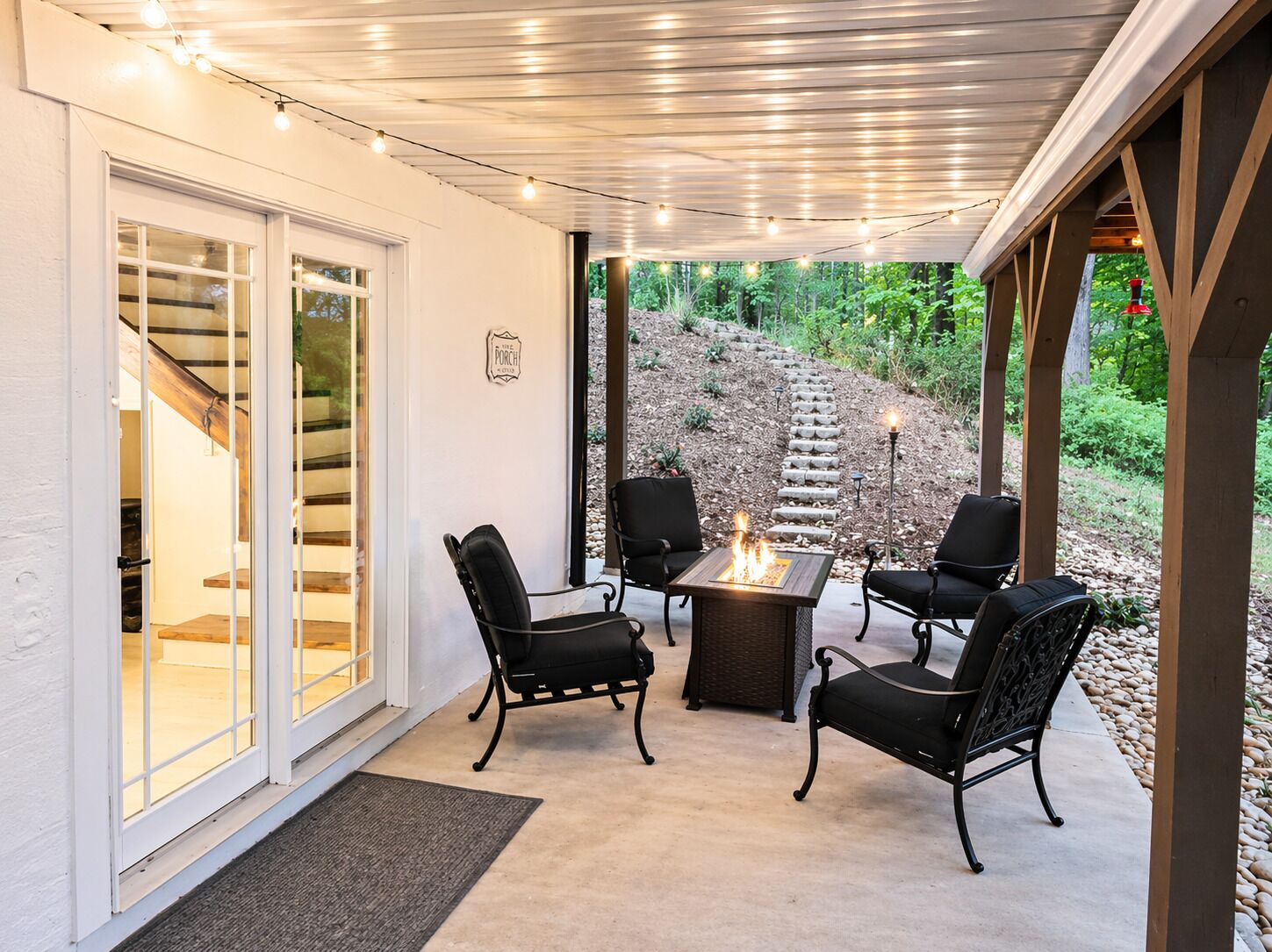 Eine Terrasse im Freien mit Feuerstelle, schwarzen Stühlen und einer Pergola mit Lichterketten.