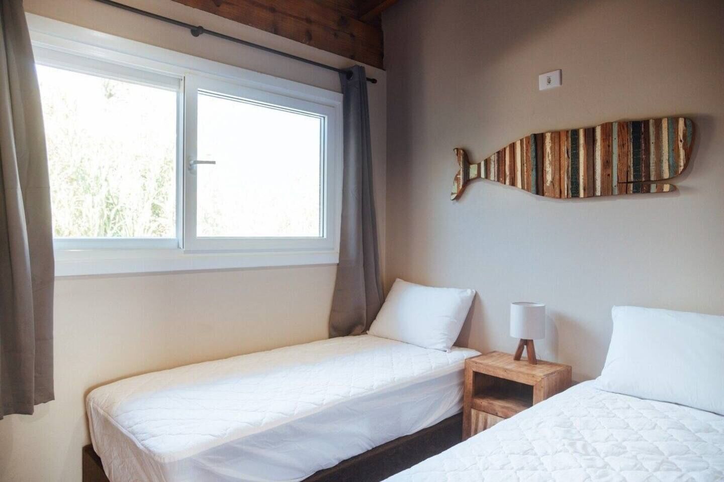 A bedroom with two beds, a window, and a wall-mounted wooden artwork.