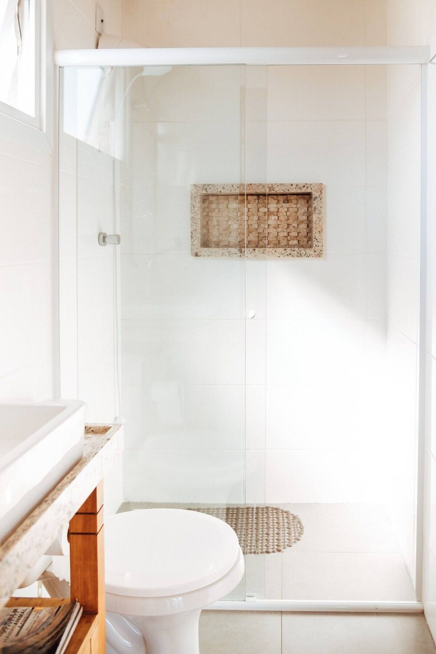 Un baño con ducha envuelta en vidrio, inodoro blanco y tocador de madera.