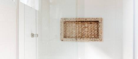 Un baño con ducha envuelta en vidrio, inodoro blanco y tocador de madera.