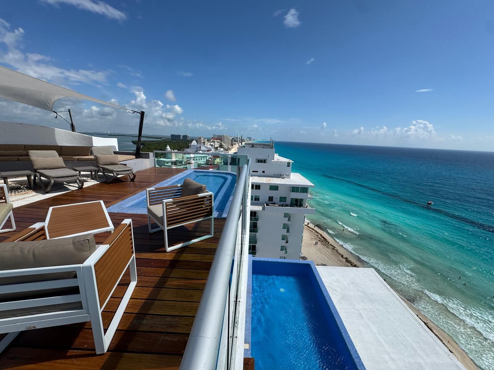 A deck with a pool, lounge chairs, and a view of the ocean.