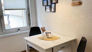 A dining area with a white table, black chairs, a black pendant light, a small potted plant, and a wall-mounted sign with the phrase "this is our happy place." - Bergluft Appartements - Weisshorn (Zermatt)