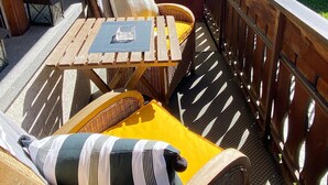 A wooden deck with wicker furniture, including a table and chairs, and a yellow cushion. - Bergluft Appartements - Weisshorn (Zermatt)