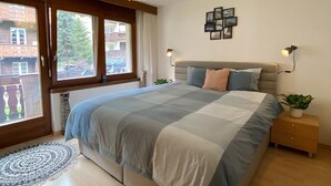 A bedroom with a large bed, a ceiling light, a window with curtains, and a small plant on a nightstand. - Bergluft Appartements - Weisshorn (Zermatt)