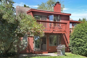 Une maison rouge à deux étages, dotée d’un balcon, de grandes fenêtres et d’un barbecue dans le jardin.
