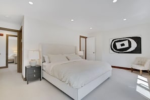 Une chambre à coucher avec un grand lit, des tables de chevet, une chaise et une œuvre d’art murale.