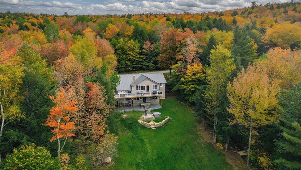 A large house surrounded by a forest with autumn foliage.