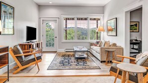 A modern living room with a sofa, coffee table, TV, and large windows.