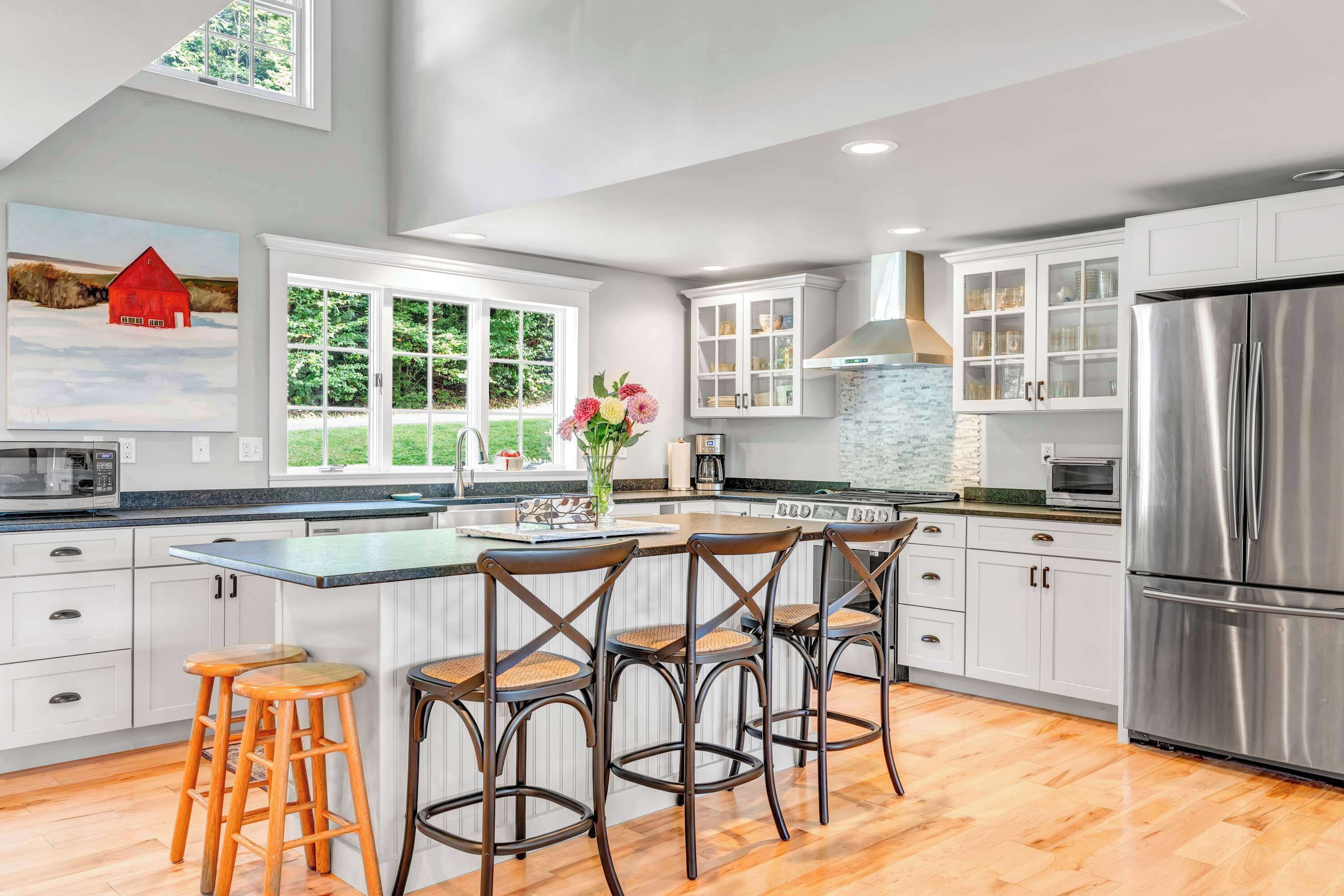 A modern kitchen with white cabinets, a stainless steel refrigerator, and a large island with bar stools.