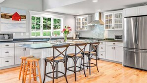 A modern kitchen with white cabinets, a stainless steel refrigerator, and a large island with bar stools.