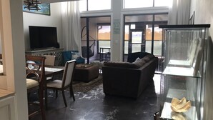 En stue med et stort fladskærms-tv, en blå sofa, en brun sofa, et spiseområde med bord og stole, samt et glasmontre.