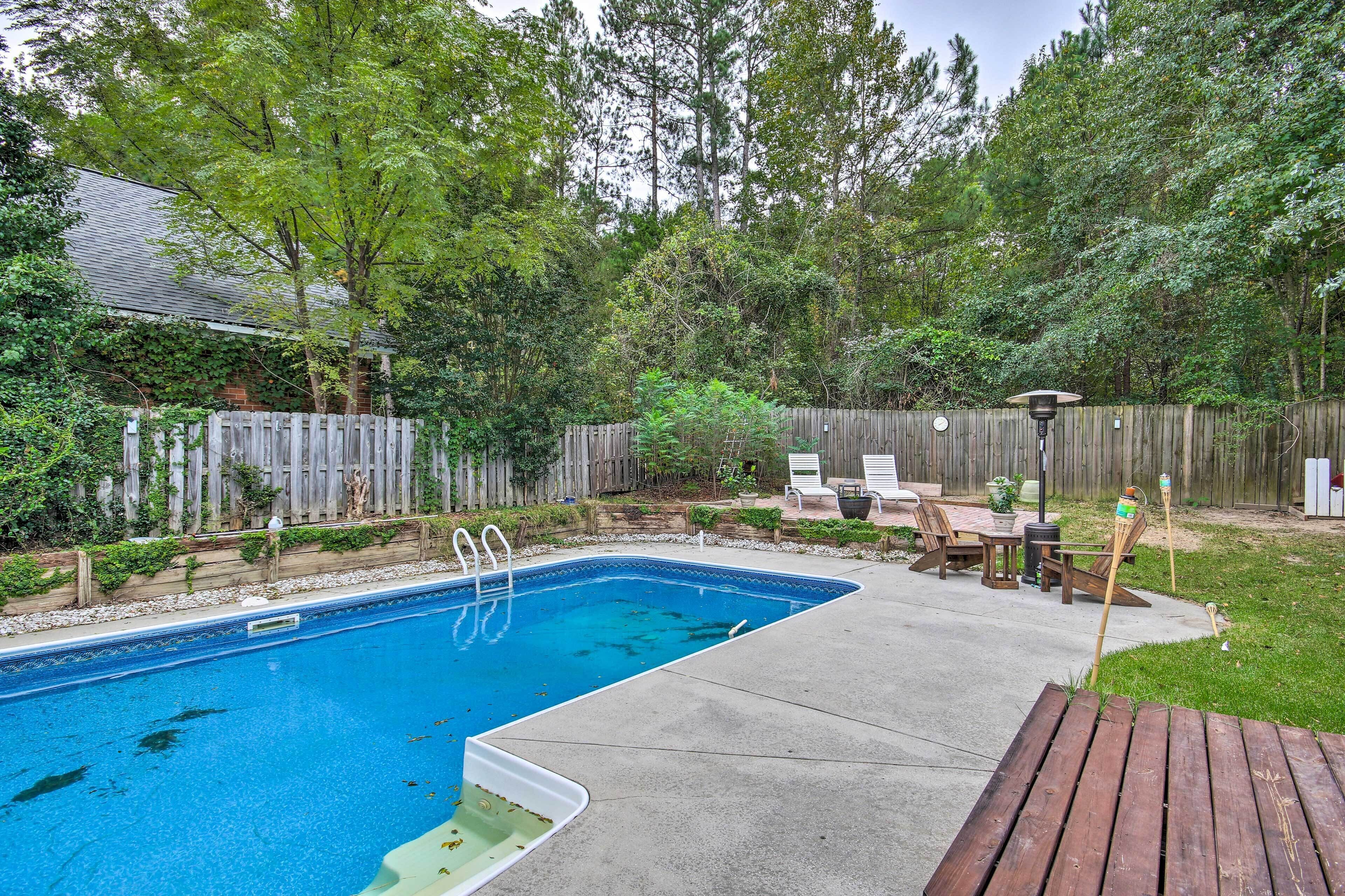 A backyard with a swimming pool, wooden deck, and outdoor furniture.