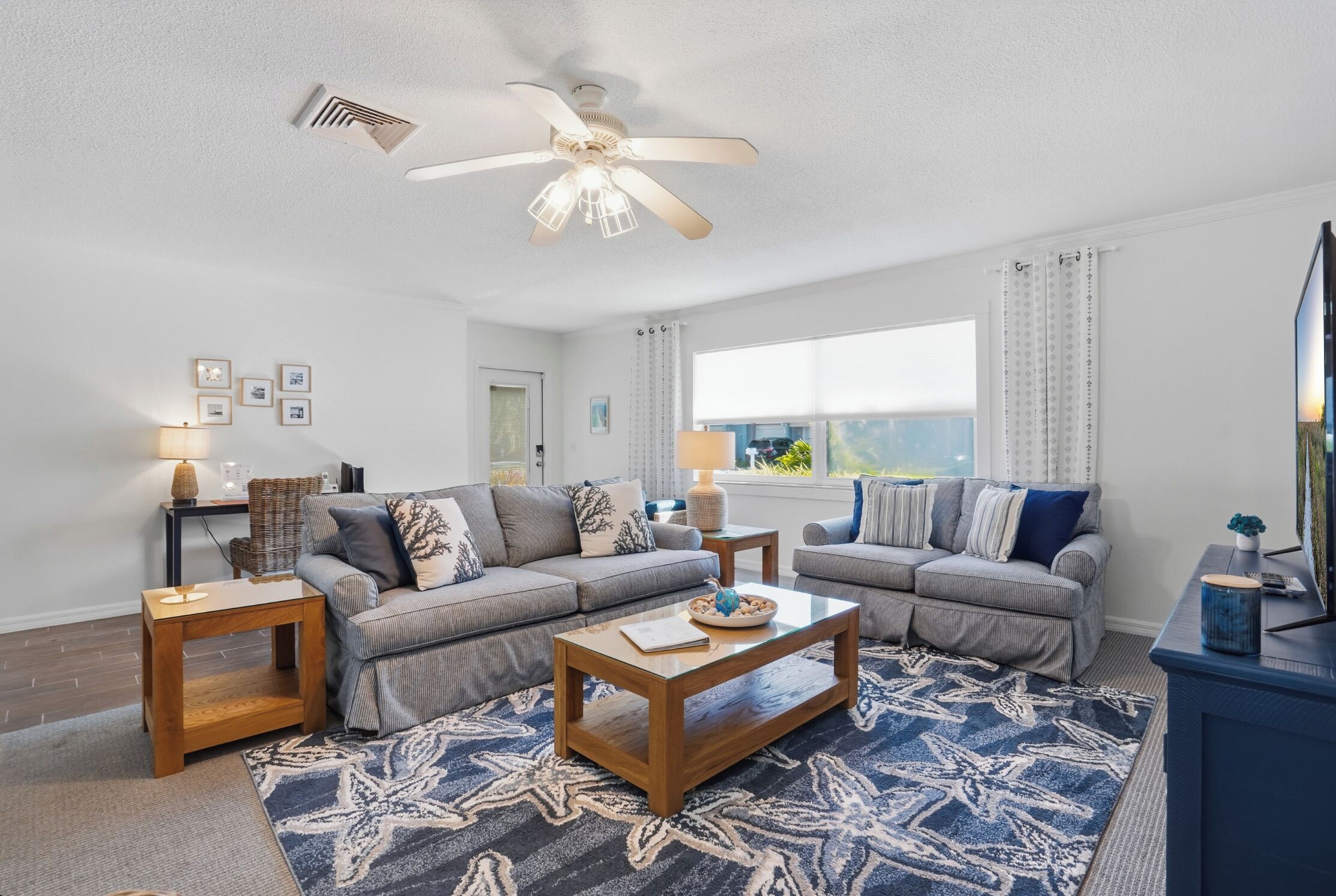 A living room with two sofas, a coffee table, a ceiling fan, and a large window with curtains.