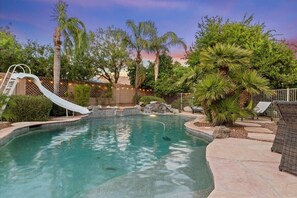 Relax by the serene pool surrounded by lush tropical plants and lounge chairs.
