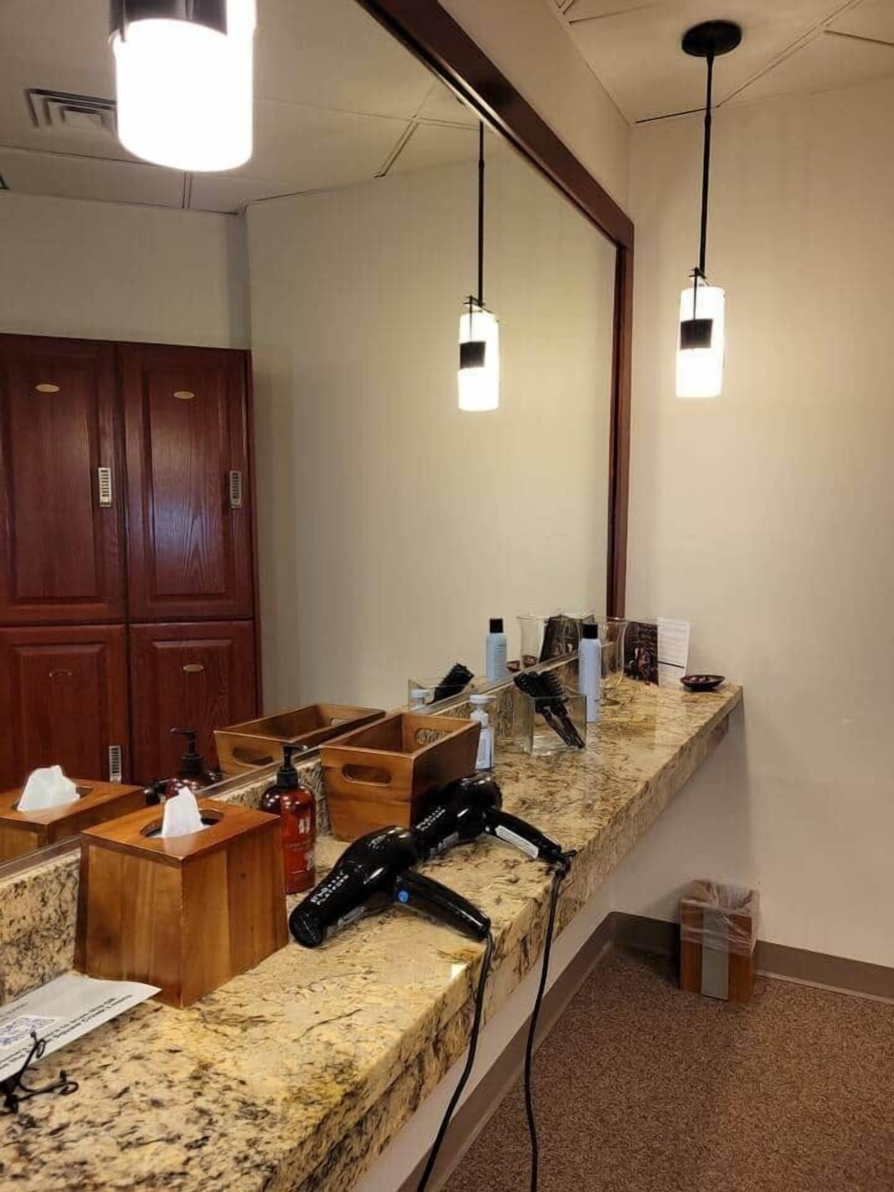 A hotel bathroom with a granite countertop, wooden cabinets, and a large mirror.