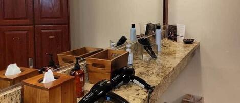 A hotel bathroom with a granite countertop, wooden cabinets, and a large mirror.