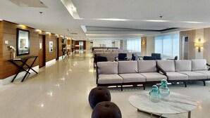 Un vestíbulo amplio con diseño moderno, que incluye una zona de estar con sofás y una mesa de centro, y un mostrador de recepción con un espejo y cuadros enmarcados.