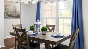 Un comedor con una mesa de madera, cuatro sillas, un farol blanco y cortinas azules.