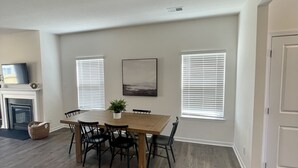A dining area with a wooden table and chairs, a fireplace, and a television on the wall. - Beautiful new home with lake view near hiking trails (Oak Ridge)