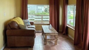 Una habitación con un sofá marrón, una mesa de madera y una ventana con cortinas.