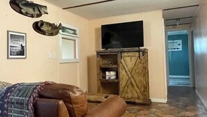 Una sala de estar con un sofá de cuero marrón, un televisor montado en la pared y un mueble de madera con estantes.