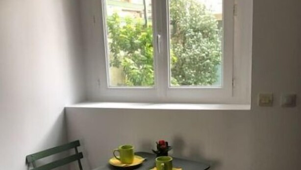 Un petit coin repas avec une table et deux chaises, une fenêtre donnant sur un espace verdoyant et une porte.
