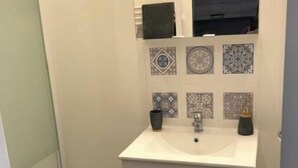 Une salle de bain avec un lavabo blanc, deux distributeurs de savon noirs, un miroir au-dessus du lavabo et des carreaux décoratifs sur le mur.