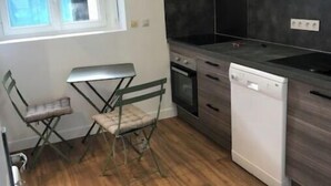 Une cuisine moderne avec des meubles en bois foncé, un four encastré et un lave-vaisselle. Une fenêtre laisse entrer la lumière naturelle, et il y a une petite table pliante avec des chaises.