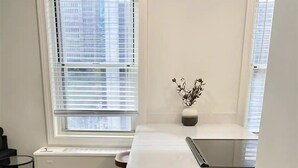Une cuisine dotée d’un long comptoir blanc, d’un four encastré et d’une fenêtre avec des stores.