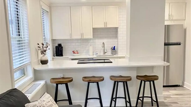 Une cuisine moderne avec des meubles blancs, un îlot central doté de tabourets et un réfrigérateur.
