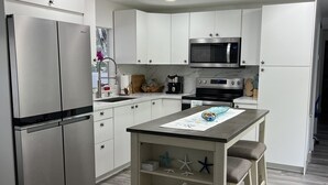 Una cocina moderna con armarios blancos, electrodomésticos de acero inoxidable y una isla central con taburetes.