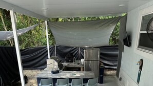 Un patio al aire libre techado con una parrilla, refrigerador y taburetes de bar.