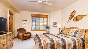 Une chambre à coucher comprenant un lit, une chaise, une commode, un téléviseur, une fenêtre et un ventilateur de plafond.