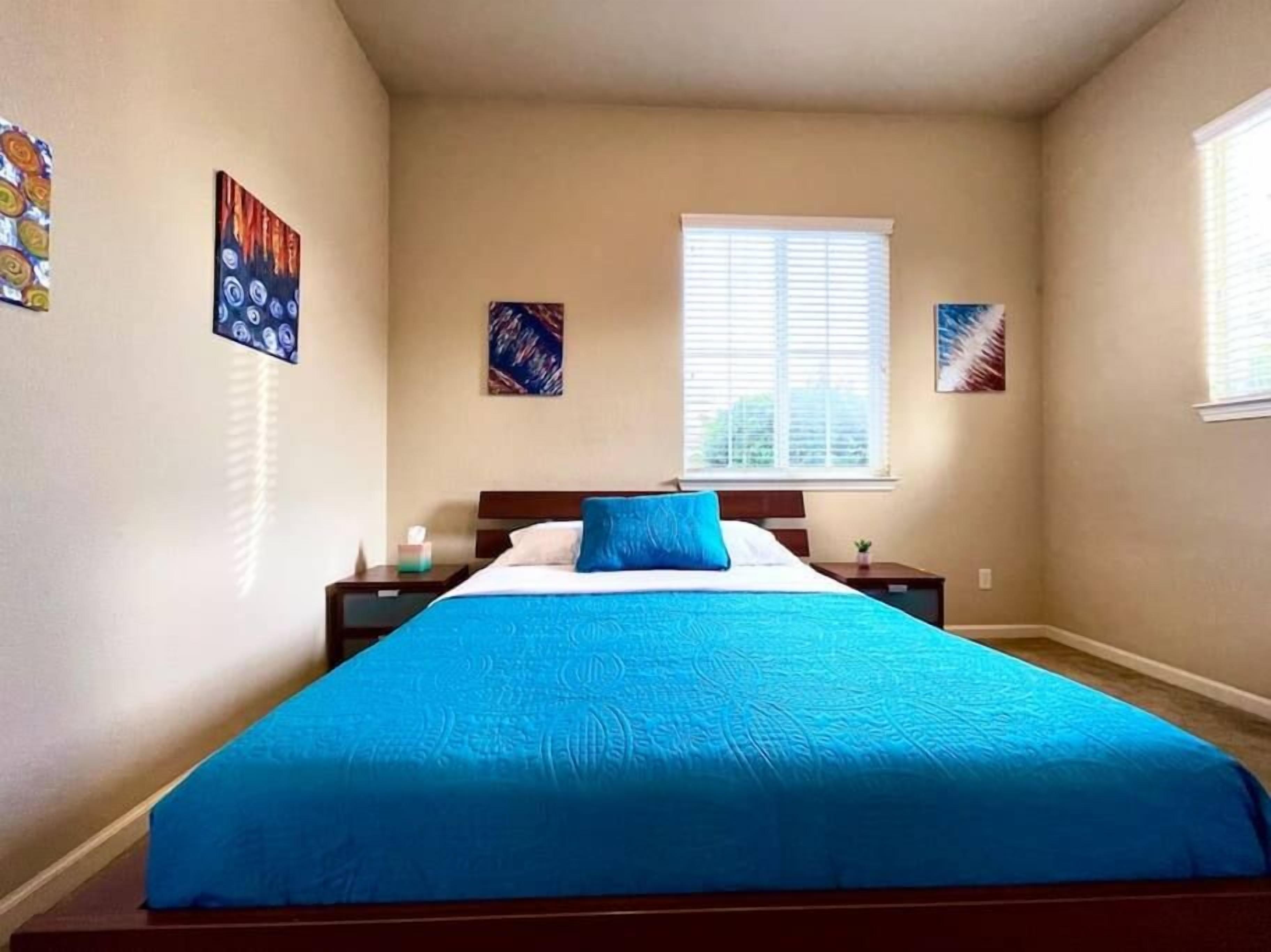 Un dormitorio con una cama, dos mesitas de noche, una ventana y decoración en la pared.