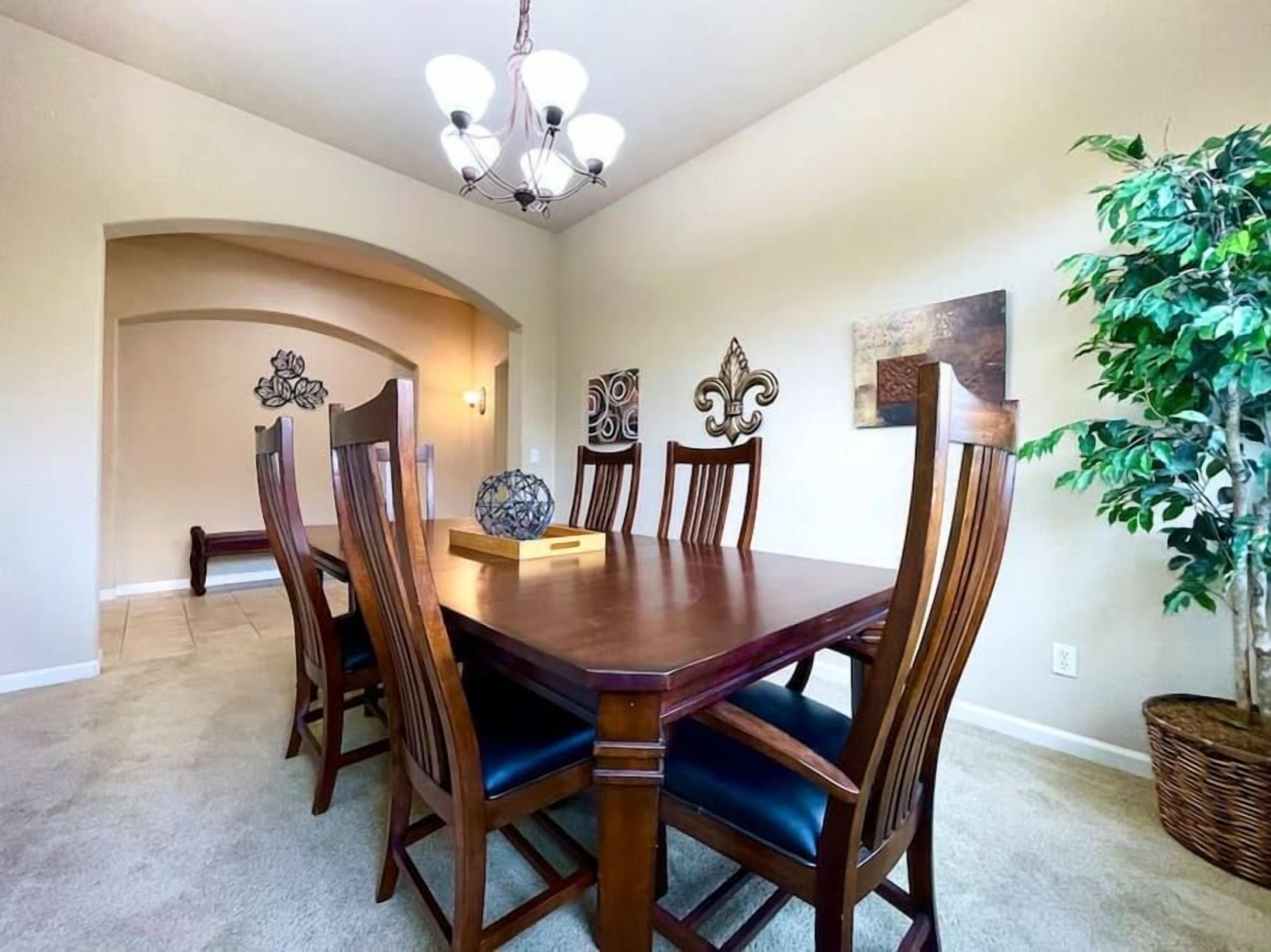 A dining room with a wooden table and chairs, a chandelier, decorative wall art, and a potted plant.