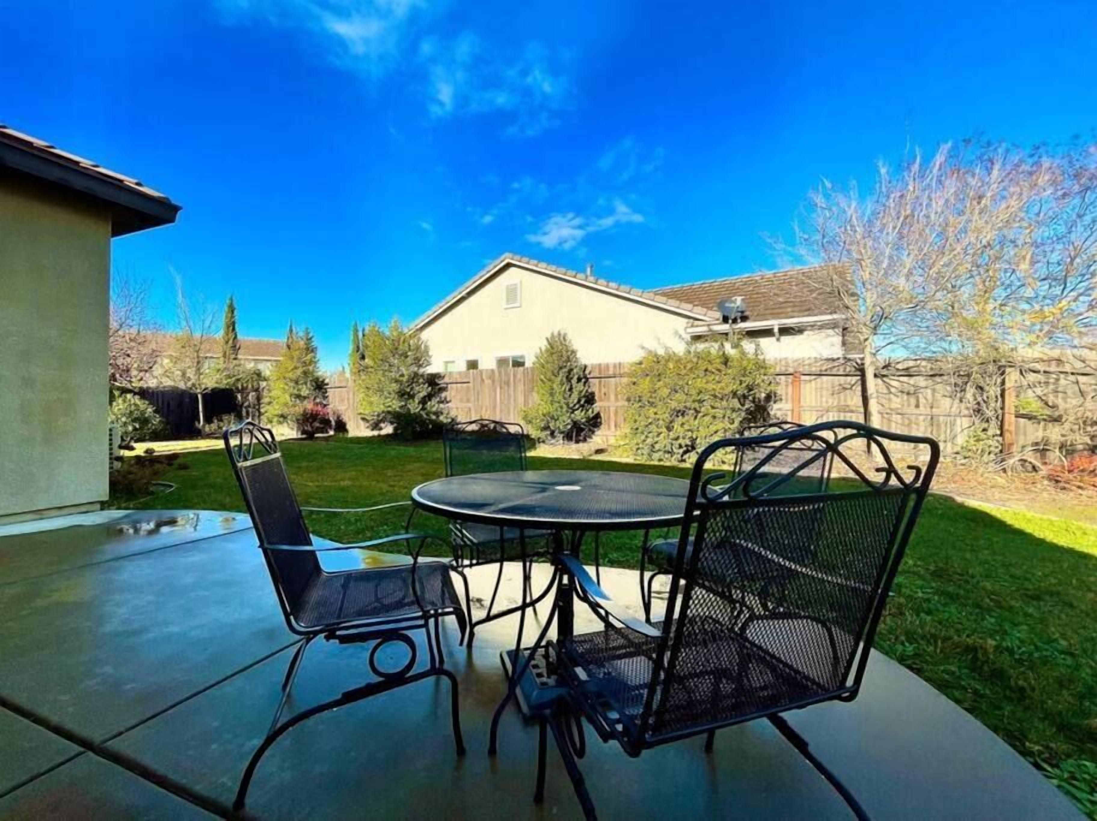 Eine Terrasse mit einem runden Tisch und Stühlen, einem Betonboden und einem Haus im Hintergrund.