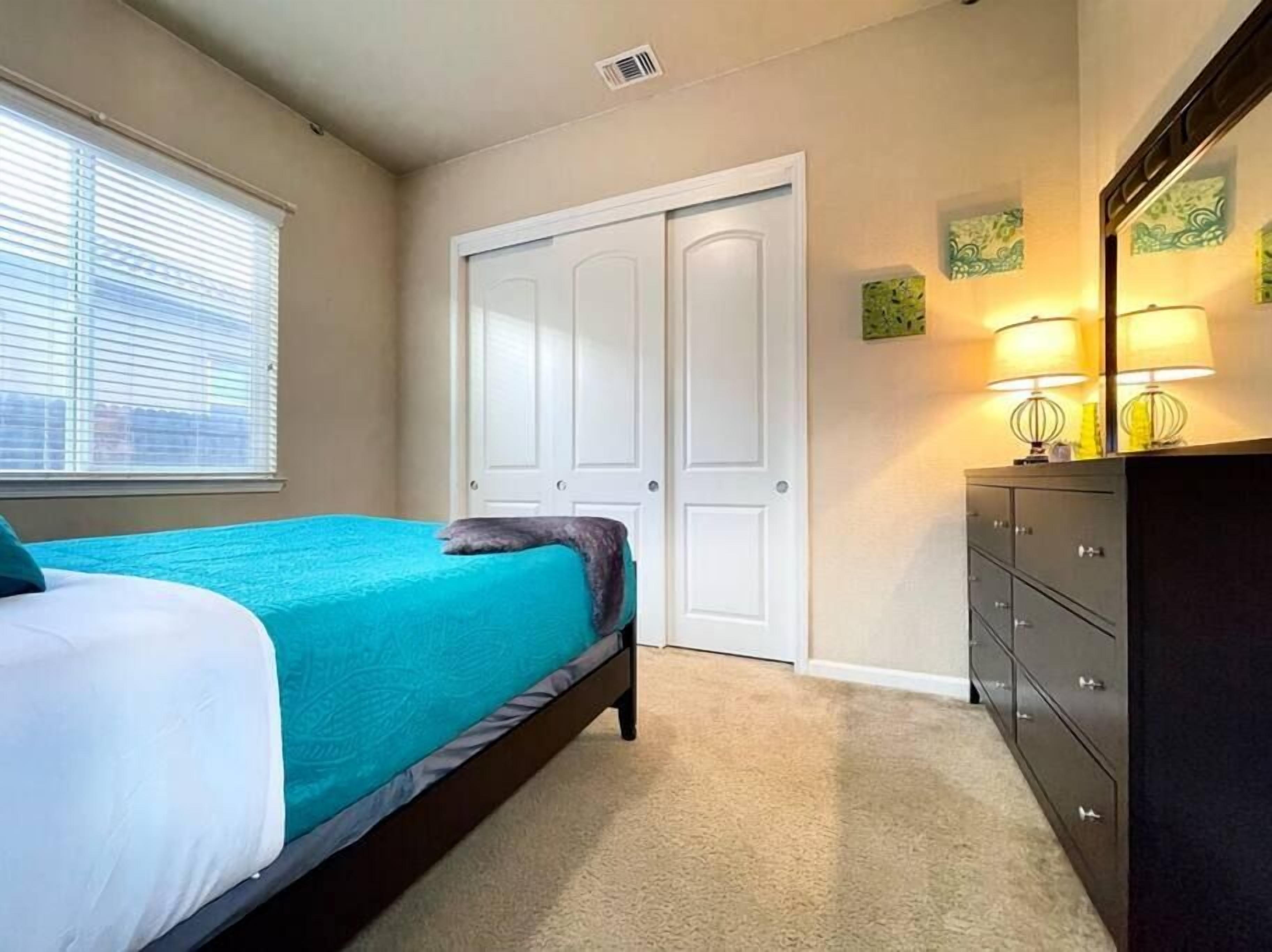 Une chambre à coucher avec un lit, une commode, un placard et une fenêtre avec des stores.