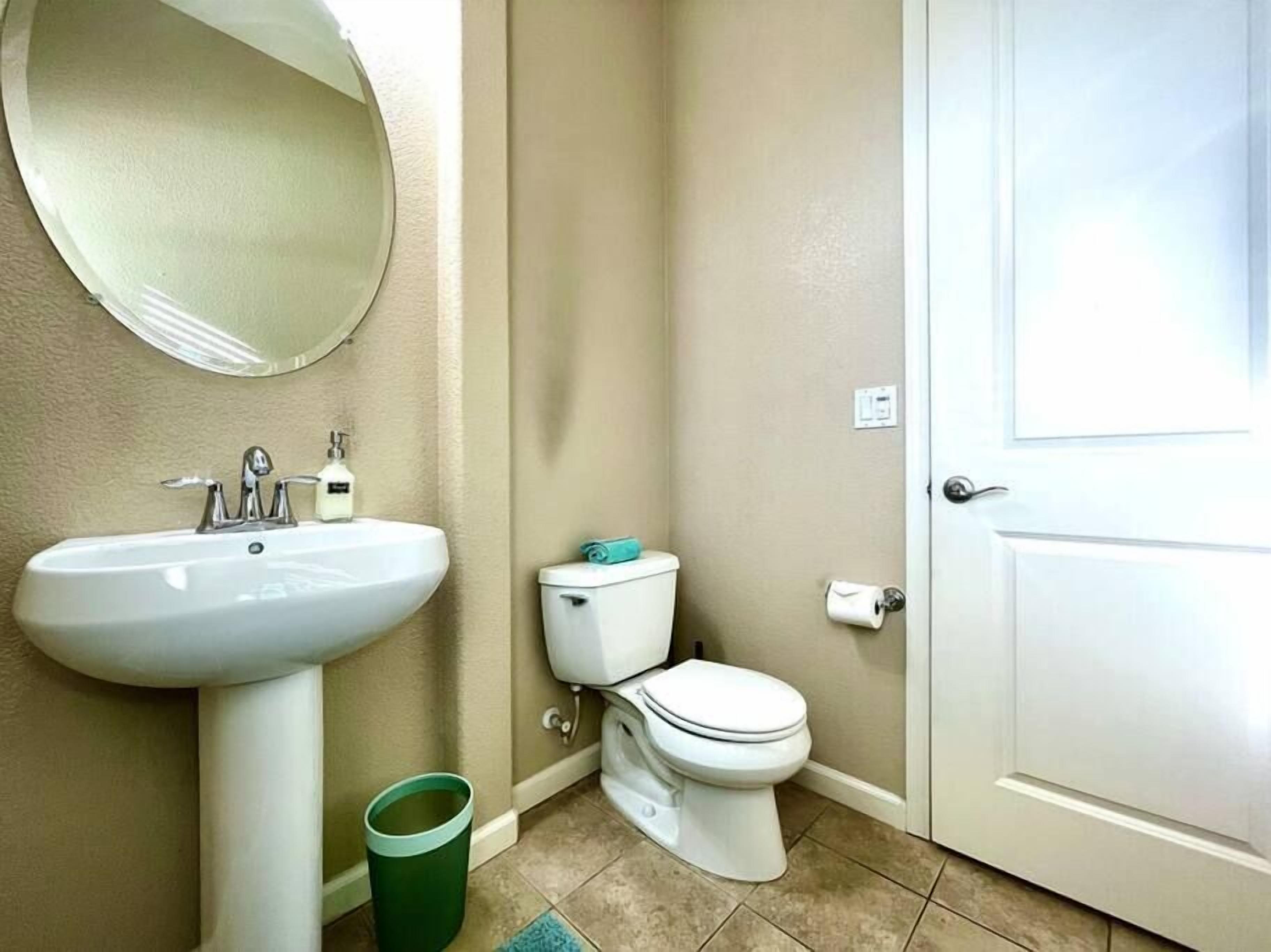 A bathroom with a white sink, a toilet, a mirror, and a door.