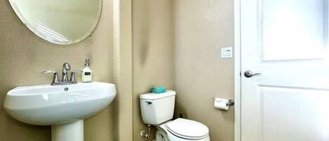 Een badkamer met een wit wastafel, toilet, spiegel en deur.
