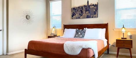Un dormitorio con cama de madera, dos mesitas de noche con lámparas, un cuadro de paisaje urbano en la pared y una decoración de sol en la pared.