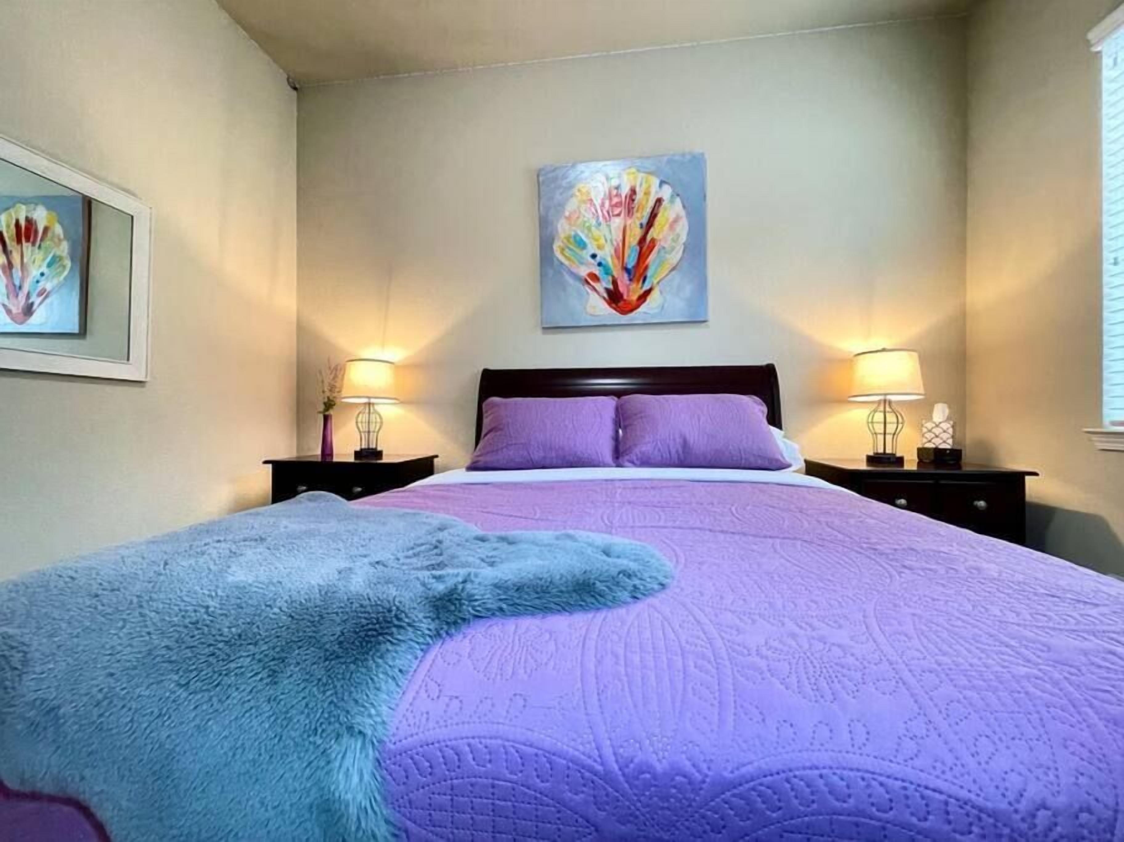 Un dormitorio con cama, dos lámparas de noche, un cuadro en la pared y un suave plaid.