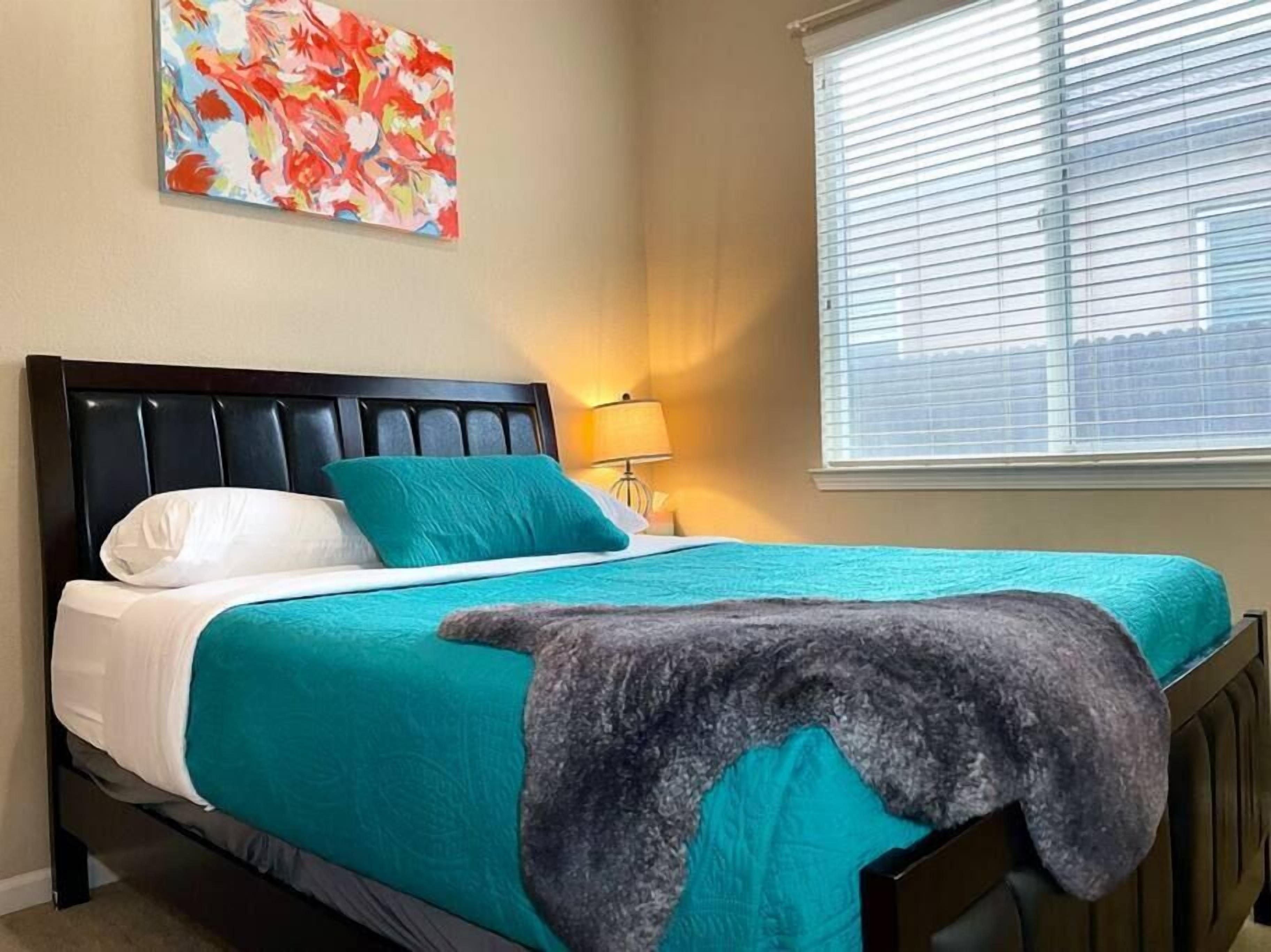 A bed with a headboard, a pillow, a blanket, and a wall-mounted lamp.