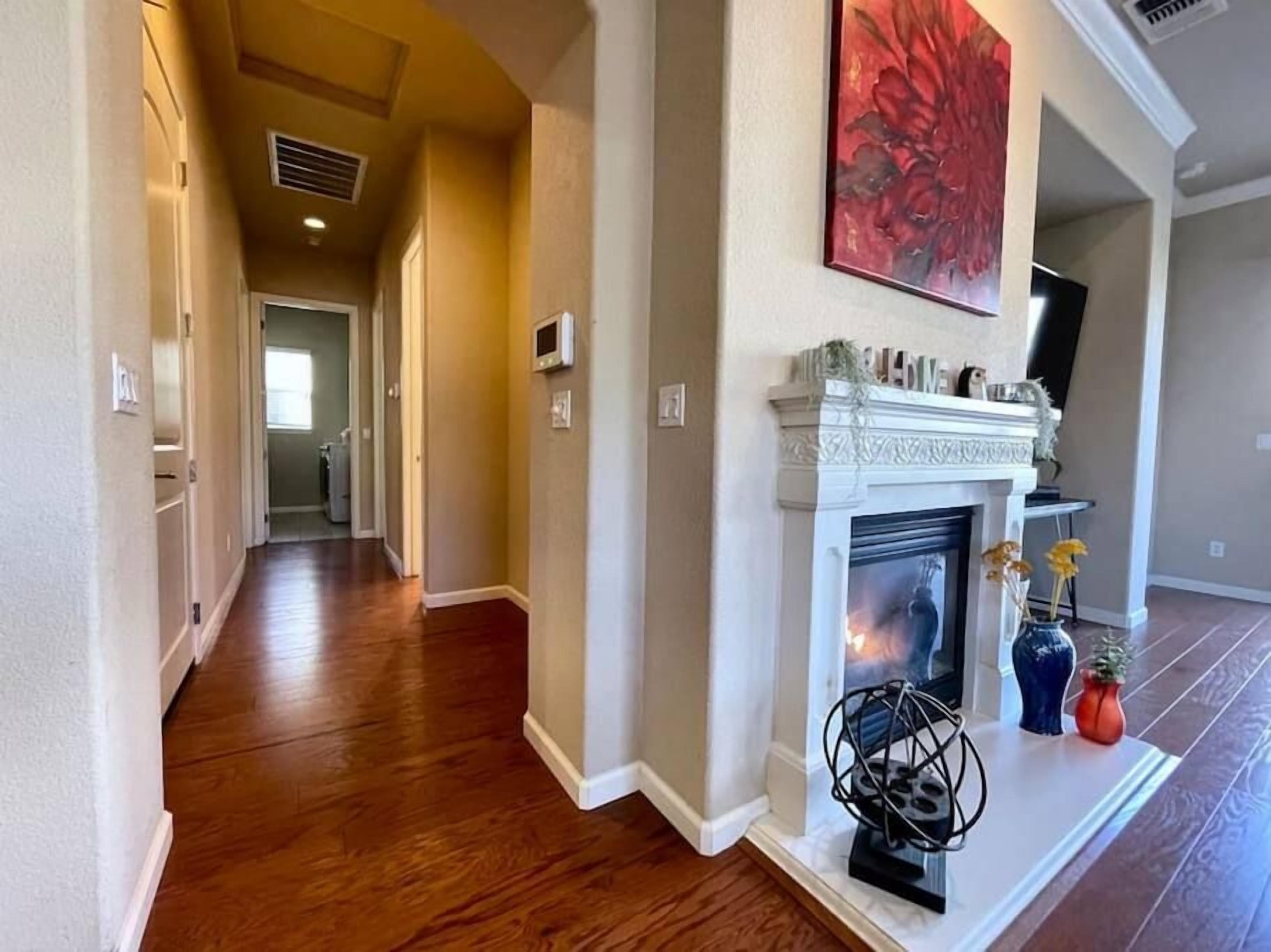 Un couloir doté d’un parquet en bois, d’une cheminée agrémentée d’objets décoratifs et d’un tableau accroché au mur.