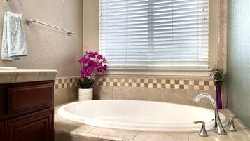 Un baño con bañera, un perchero, una ventana con persianas y una planta en maceta.