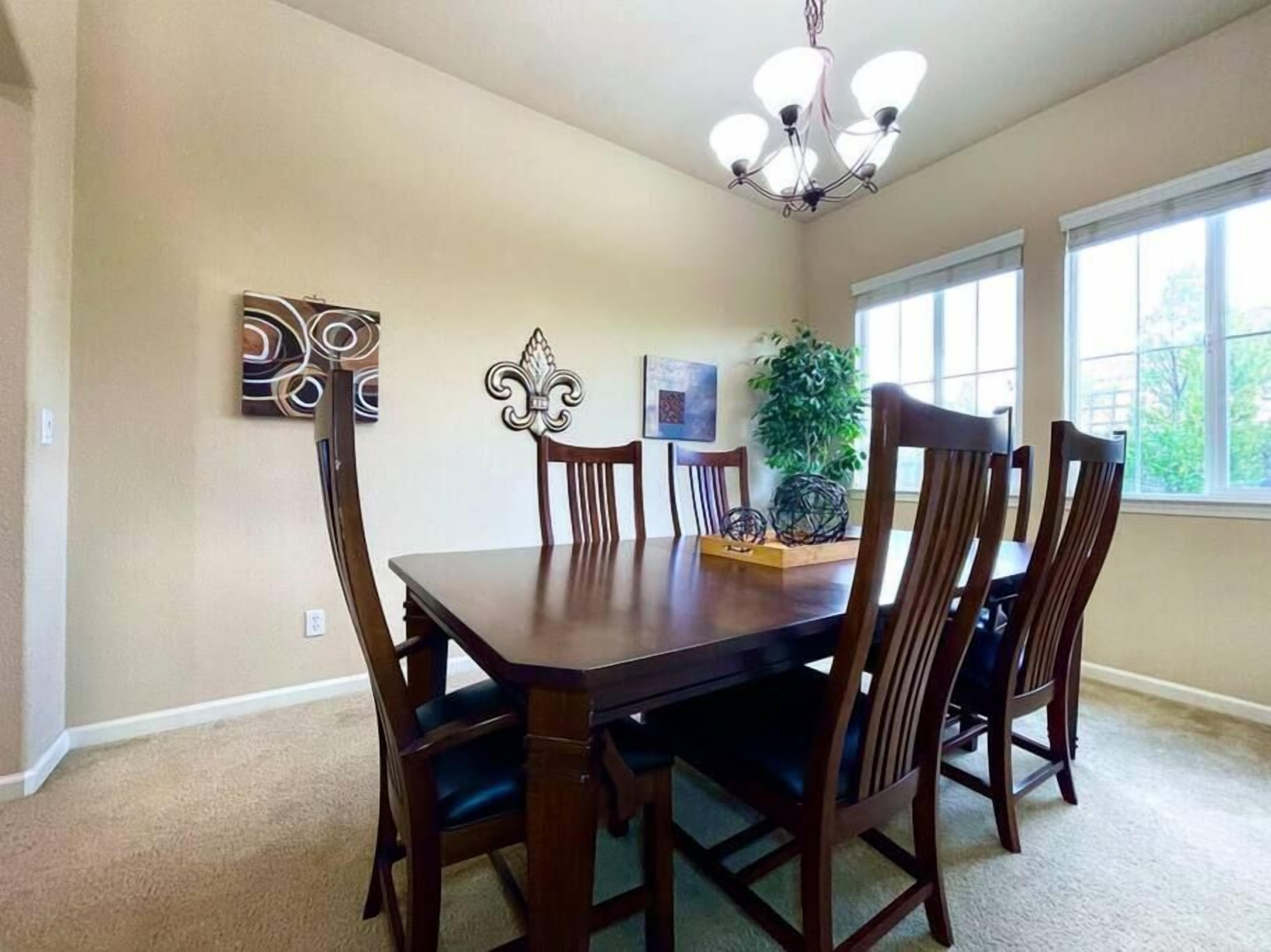 Une salle à manger avec une table et des chaises en bois, un lustre et des œuvres d’art accrochées aux murs.
